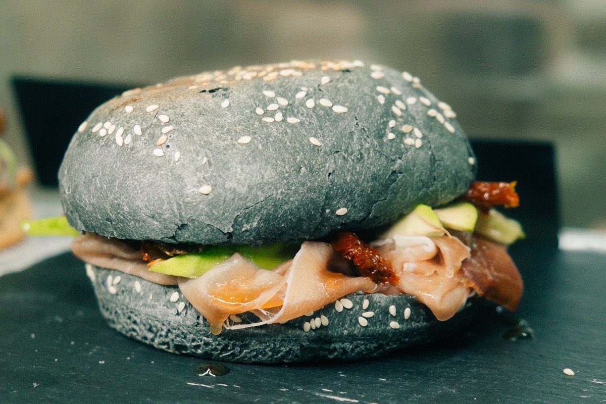 Inglima Paceville signature charcoal sesame bun filled with Parma ham, avocado and sun-dried tomato, served on slate